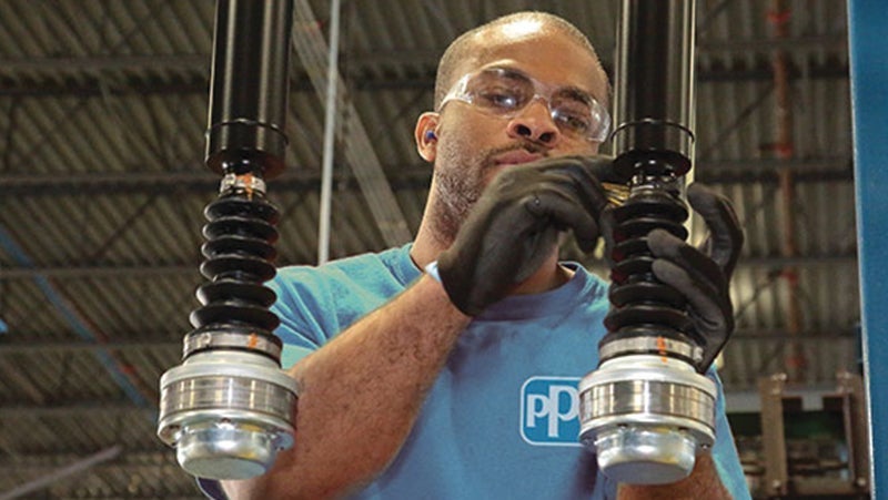 Worker in blue shirt lifting heavy industrial machinery parts in a factory setting