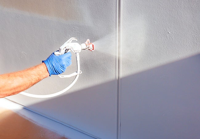 Touching up paint using a white spray gun wearing a blue protective glove