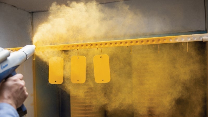 Worker applying yellow powder coating to metal parts in a workshop