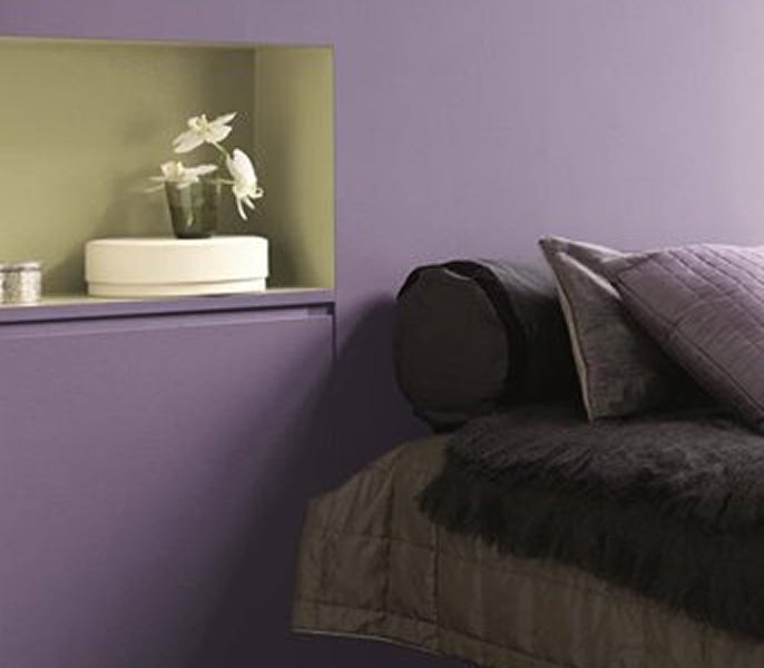 A purple wall with a shelf and a bed