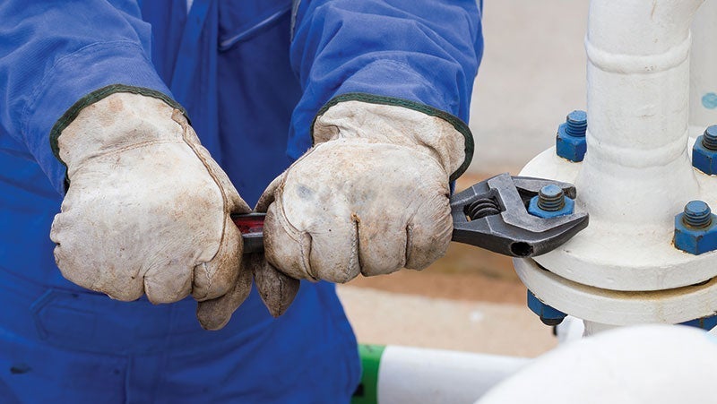 Close-up of a worker's hands in protective gloves using a wrench on industrial piping