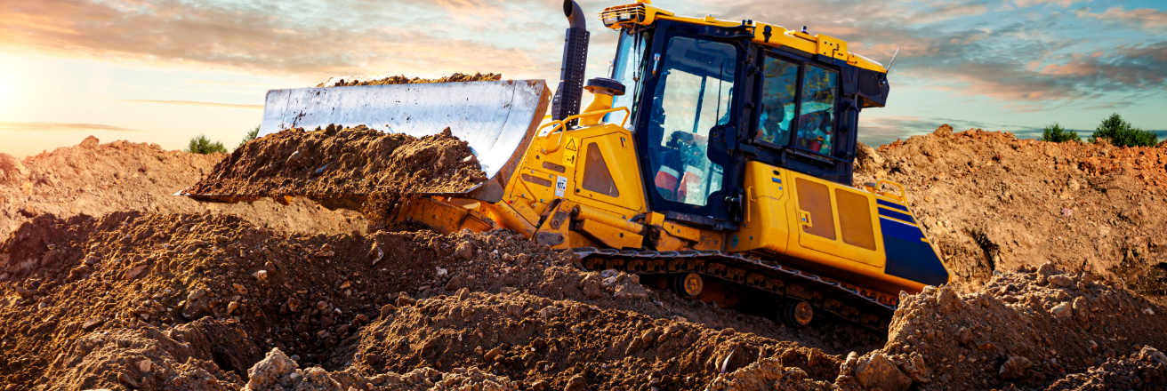 Yellow earth moving equipment plowing dirt outdoors