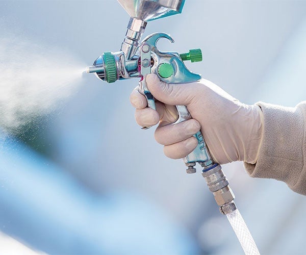 Hand holding a green metal spray gun spraying light liquid coating
