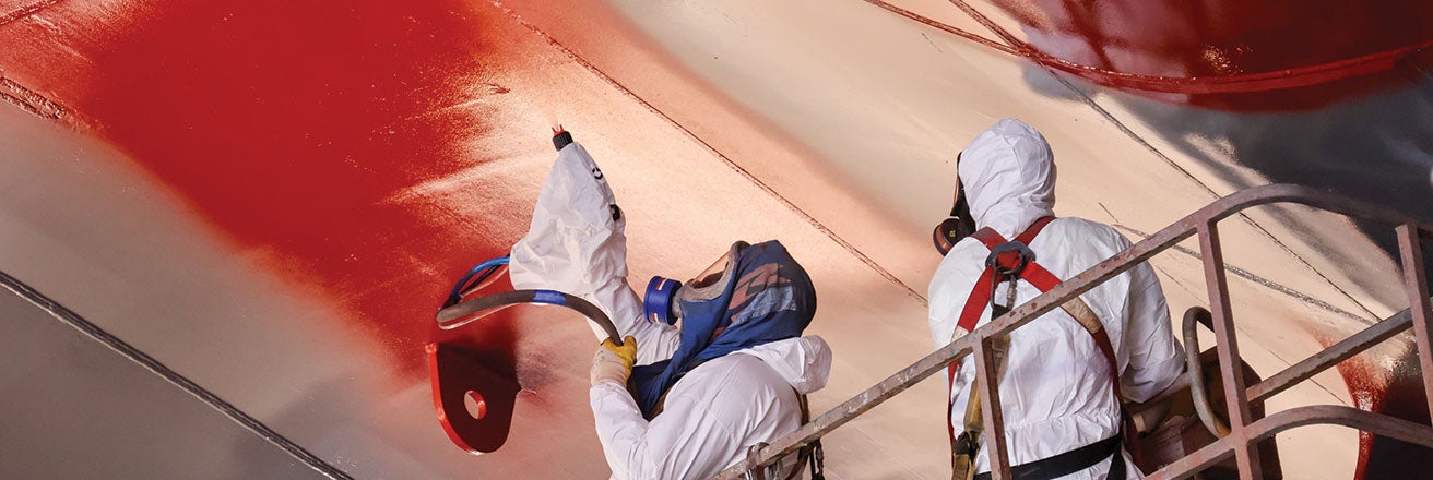 Workers in PPE spraying ship hull with red SIGMAGLIDE coating