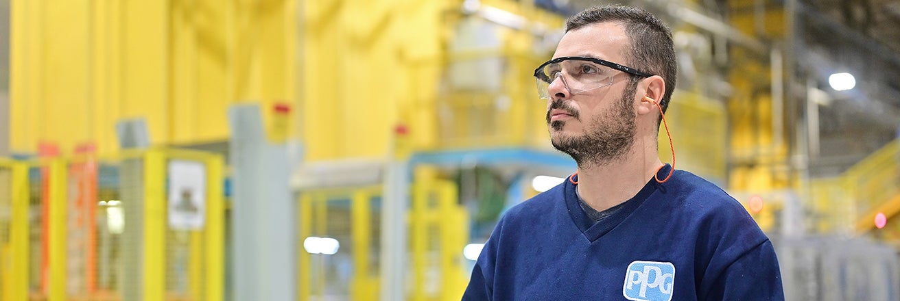 Male PPG employee wearing PPE taking notes on clipboard in factory
