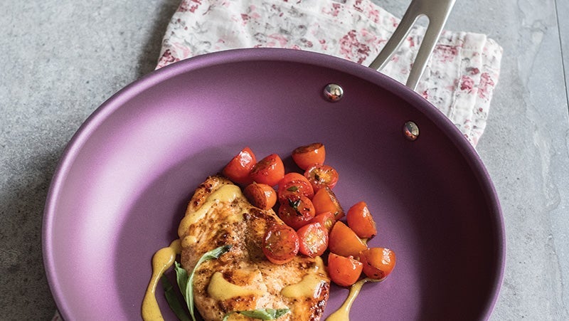 Grilled chicken breast topped with cherry tomatoes in a purple non-stick skillet on a gray countertop