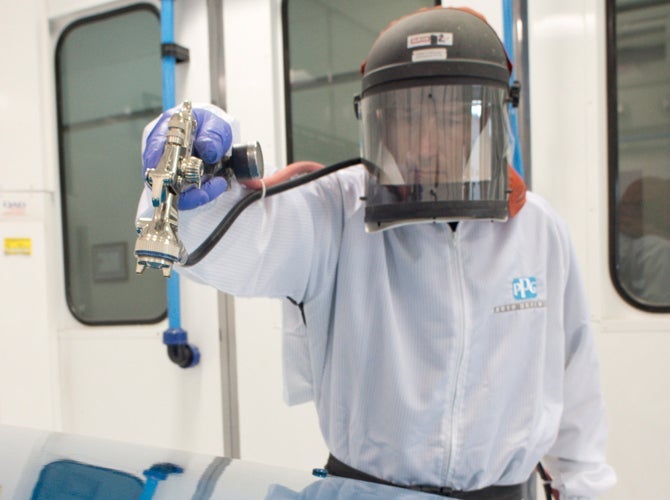 PPG worker in PPE using spray gun in booth