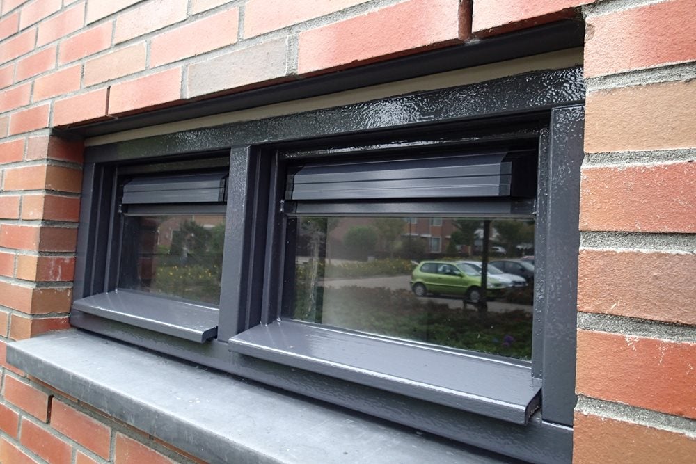 Een raam met zwarte bies en een groene auto op de achtergrond