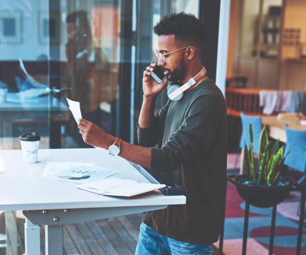 Man talking on a mobile phone at a white desk, wearing headphones around his neck