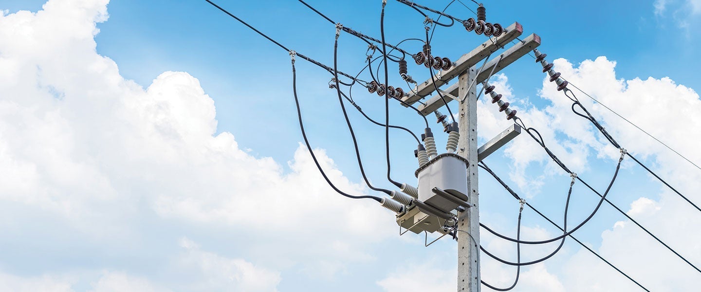 Detailed view of an electricity distribution pole with multiple wires and ceramic insulators under a clear blue sky with fluffy clouds