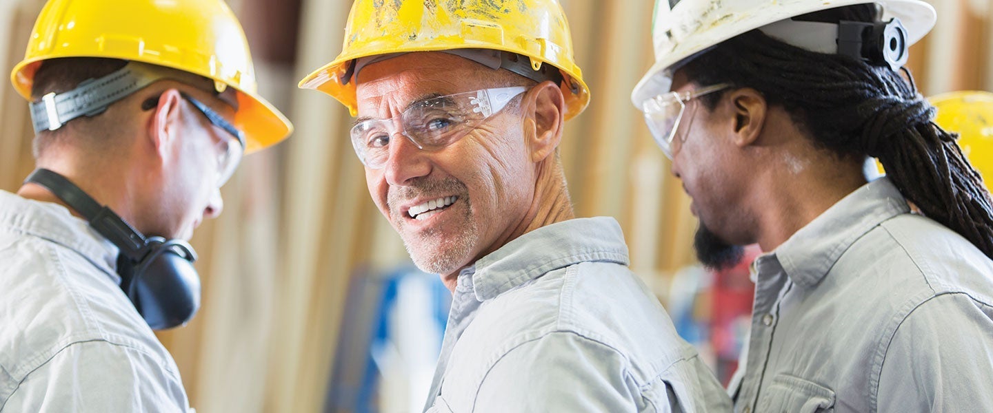 Three construction workers wearing hard hats and safety gear, engaged in discussion on a construction site