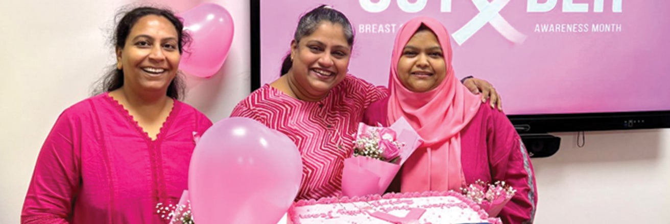 Group of ladies holding pink cake to celebrate breast cancer awareness month