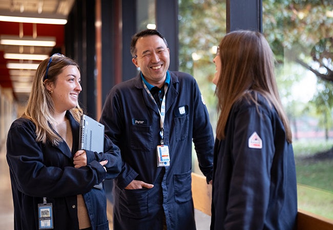 Three colleagues chatting and smiling in blue PPG overalls
