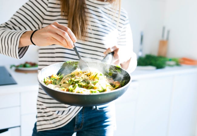 Lady in a white and blue striped top cooking in a grey spatter fry pan