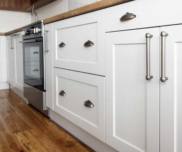 White wood kitchen units with silver handles and oven on wooden flooring