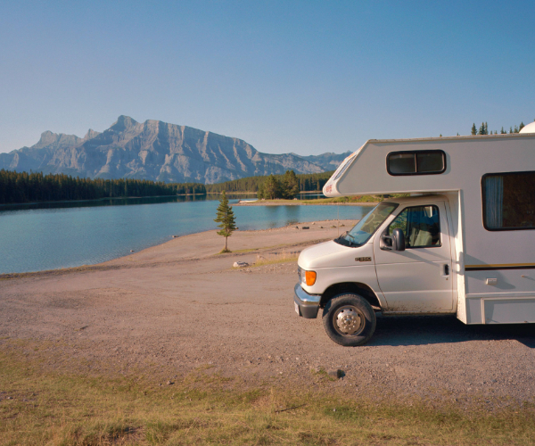 White campervan parked at the side of a lake set against mountains and a blue sky