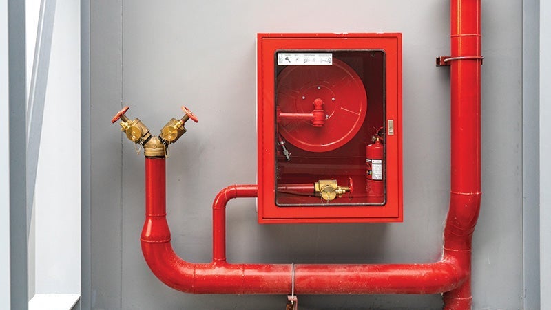 Red fire safety equipment including a hose reel, valves, and extinguisher mounted on a grey wall