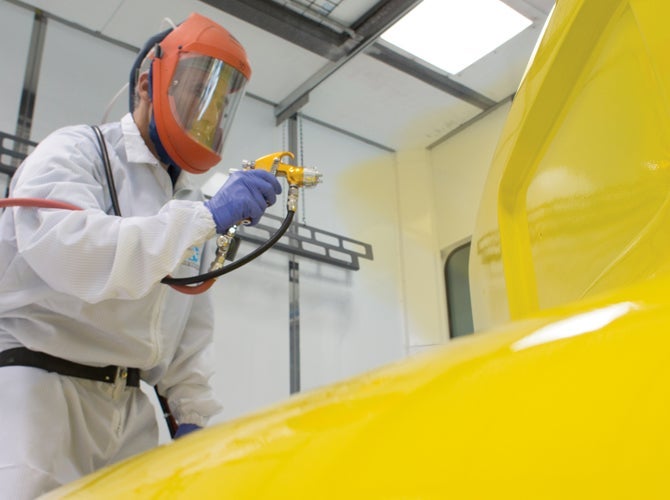 Worker in PPE spraying vehicle with yellow paint