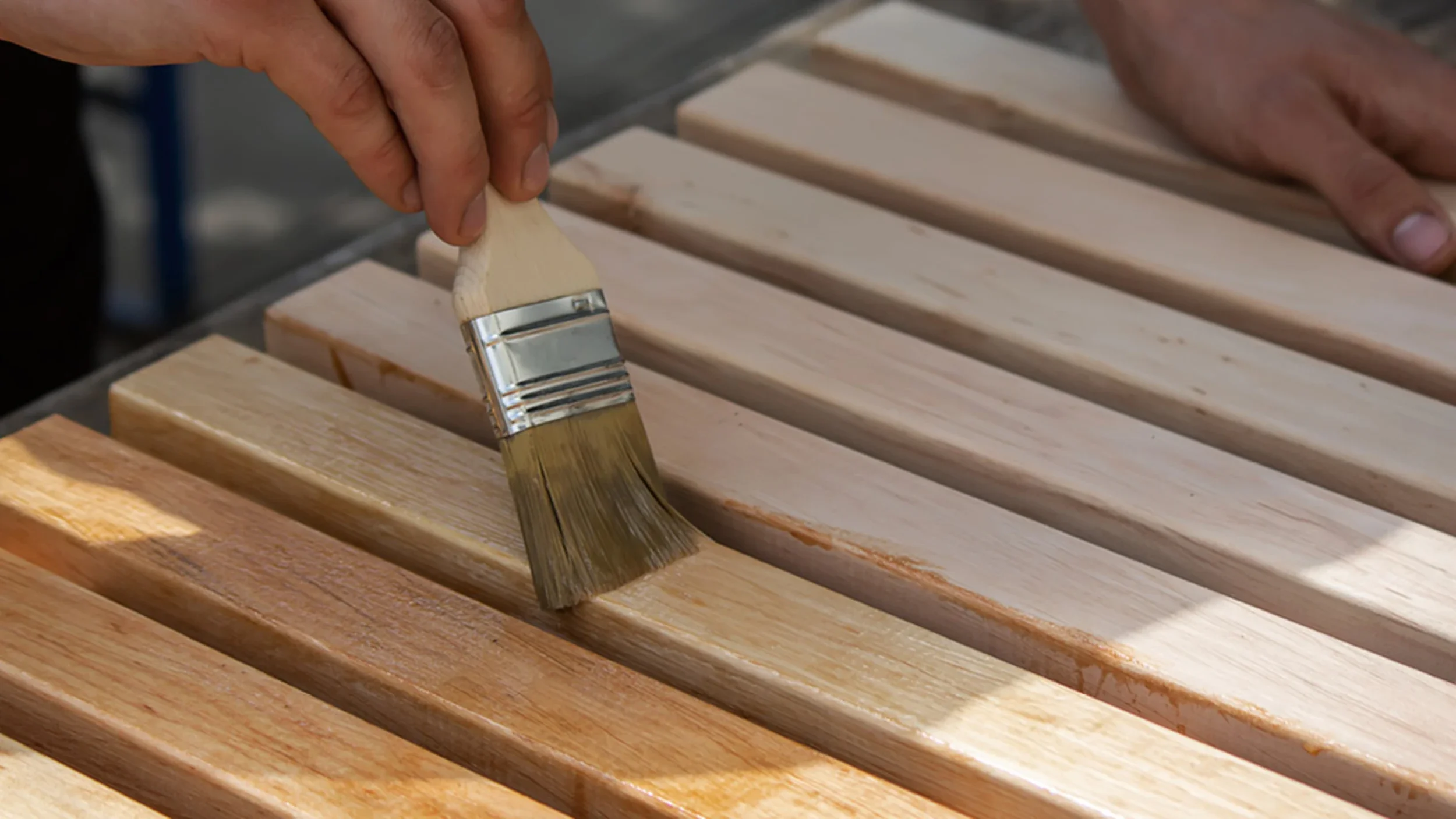 Persoon brengt met een kwast een beschermende laag aan op houten planken