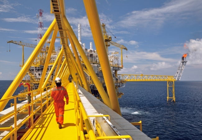 Engineer in orange coverall and white helmet inspecting machinery on an offshore platform