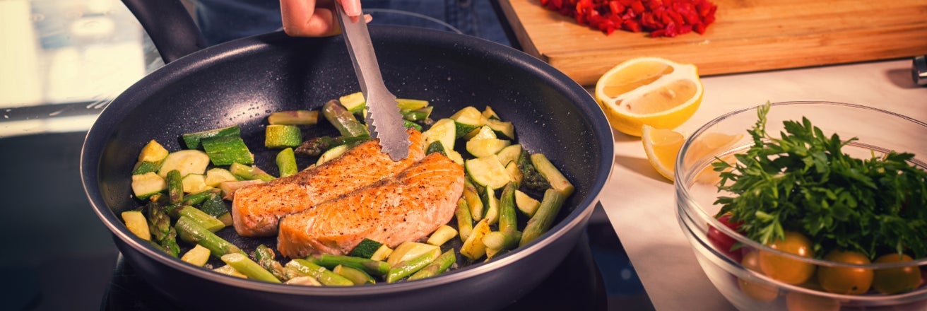 Salmon and green vegetables being cooked in a black non-stick frying pan