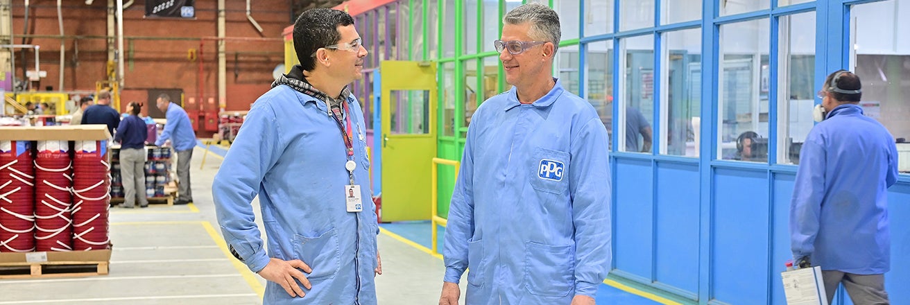 Two male workers in PPG branded overalls in discussion in large warehouse