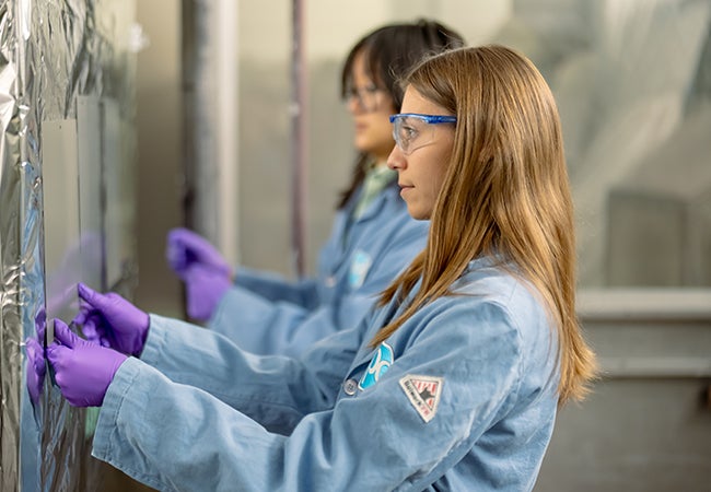Two female colleagues wearing PPE and holding swatches to wall
