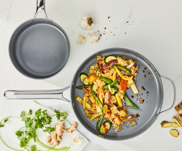 Silver interior non-stick pans cooking mixed vegetables on a cream surface