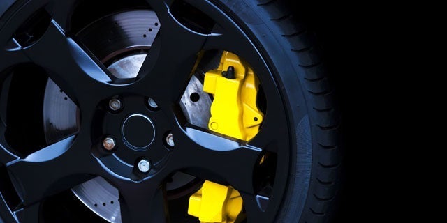 Close-up of a black alloy wheel with a yellow brake caliper on a performance car, showcasing modern automotive design and engineering