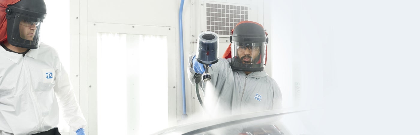 Workers in PPE spraying panel in booth