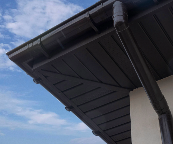 Underside of roof with guttering and drainpipe against a blue sky