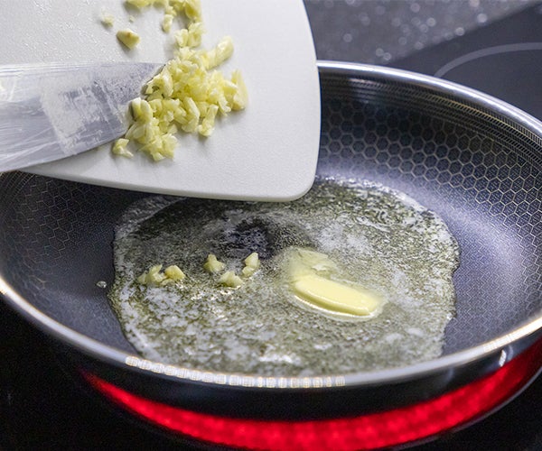 Fusion Edge black ceramic solgel coated pan on a kitchen hob with butter melting and diced vegetable being added from a white chopping board