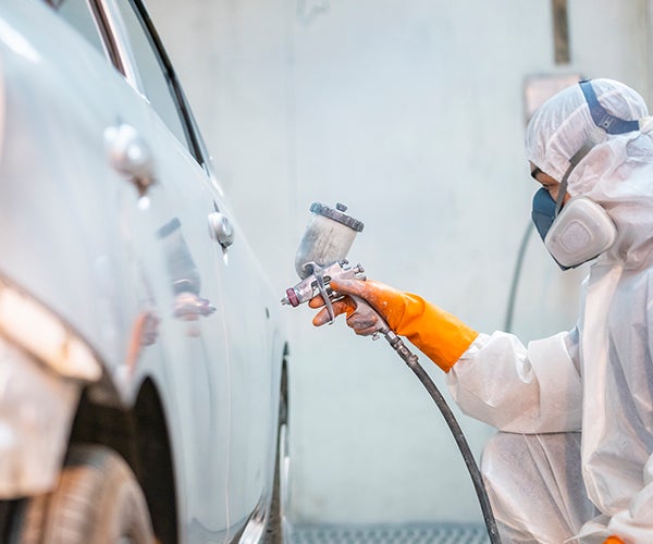Worker in PPE spraying car with spray gun