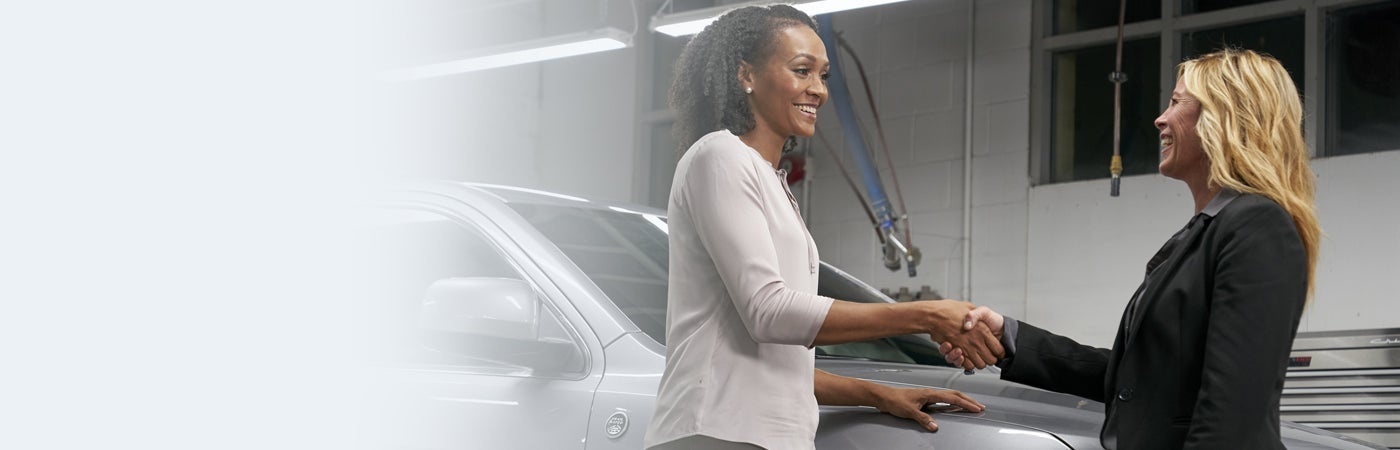 Two women shaking hands next to vehicle