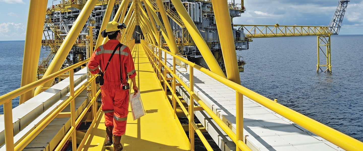 Worker in red safety suit inspecting offshore oil platform over the ocean