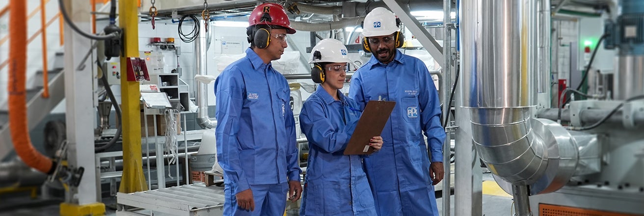 PPG workers in full PPE discussing issues next to manufacturing equipment