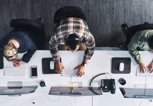 Aerial view of three people at a white desk working on white keyboards with black screens