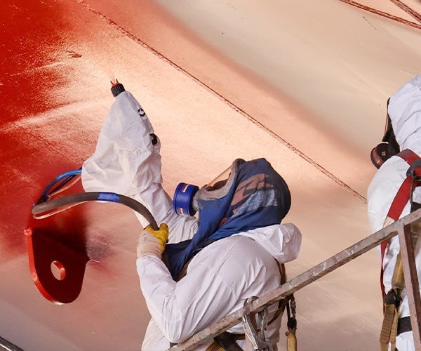 A man in white protective gear painting a red wall