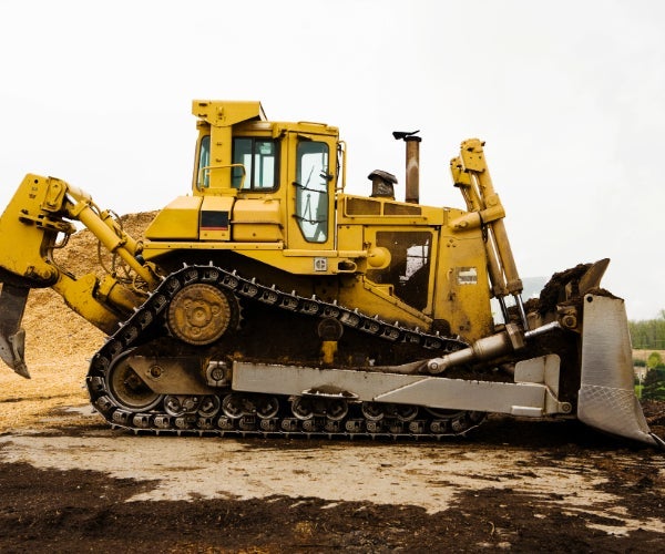 Yellow bulldozer in a quarry environment in front of piles of sand and ground dirt