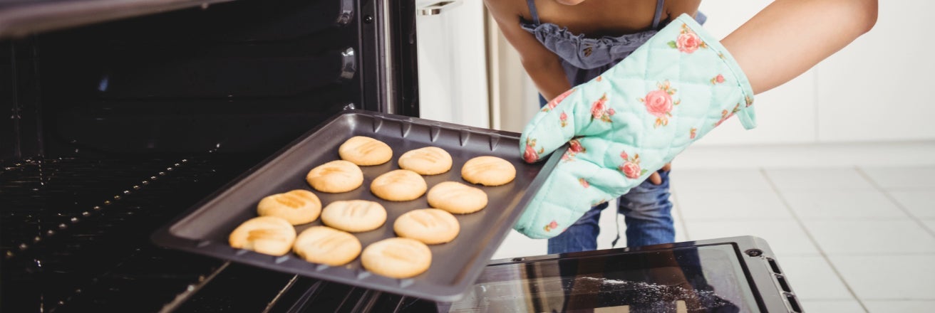 Mother and daughter taking baked cookies out of the oven