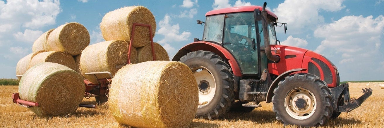 Tractor coated with red paint alongside bales of hay