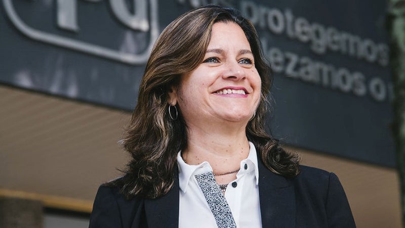 Close-up of a professional woman wearing a blazer and white shirt, standing in front of a business sign