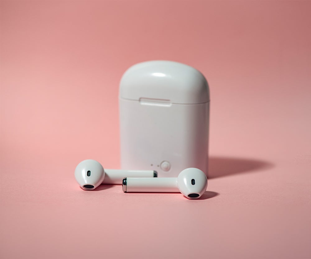 Cream airpod buds with case set against a pink background