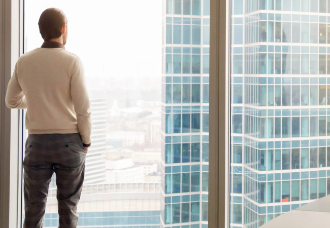 Male architect in an office looking through a window at a building with PPG’s aluminum extrusion coatings protection.