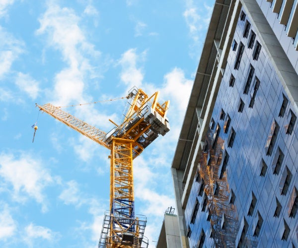 Looking up at a crane set against a blue sky next to a tall building