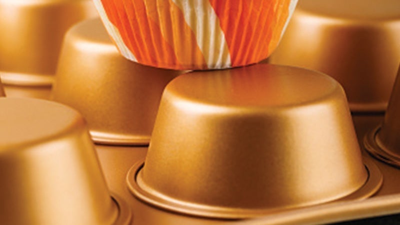 Close-up view of golden coffee capsules in a tray, with one capsule wrapped in an orange liner