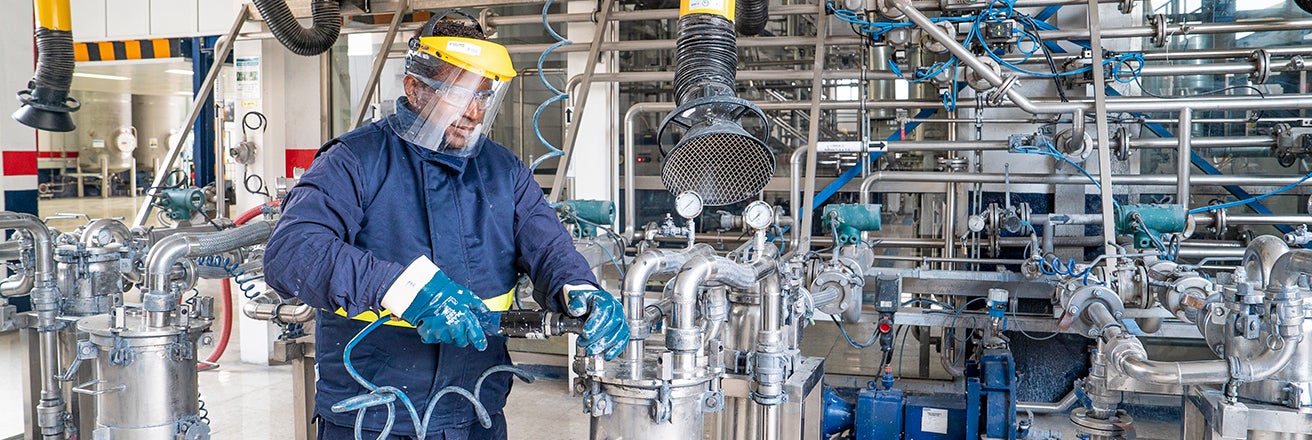 Worker in factory wearing PPE using powered tool on pipe work