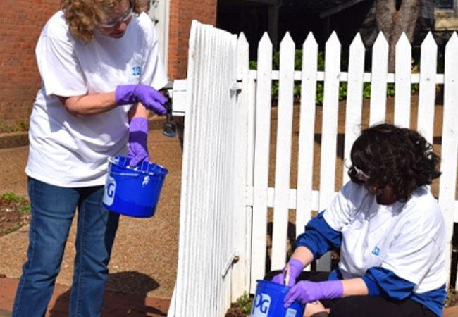 two women painting fence white in PPG paint bucket 