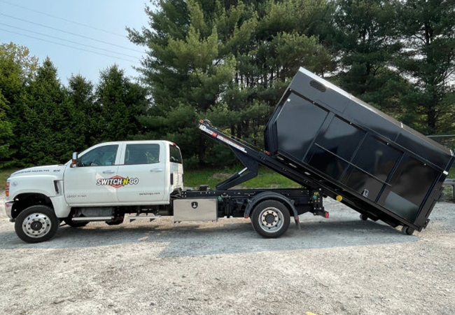 Switch-N-Go vehicle with a white truck and black lifted trailer against a green forest