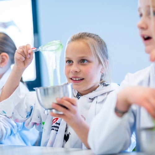 A group of girls in lab coats mixing green liquid